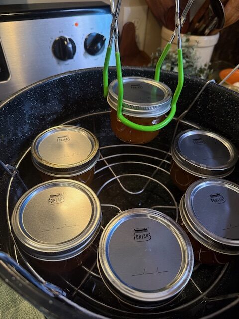 Lowering pear jam into water bath canner