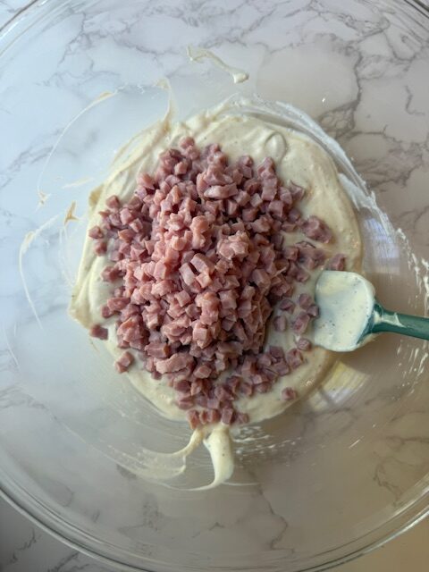 Diced ham and creamy mixture in clear mixing bowl