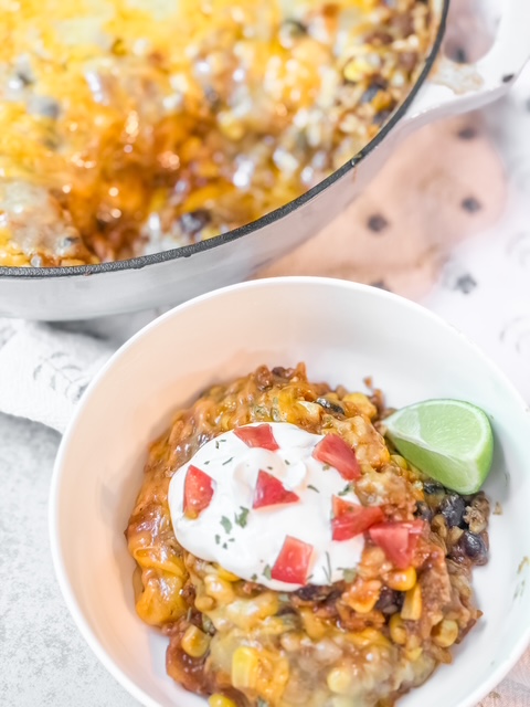 Mexican Beef and Rice Skillet served in white bowl with sour cream and lime