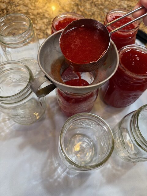 ladling strawberry lemonade concentrate into mason jars